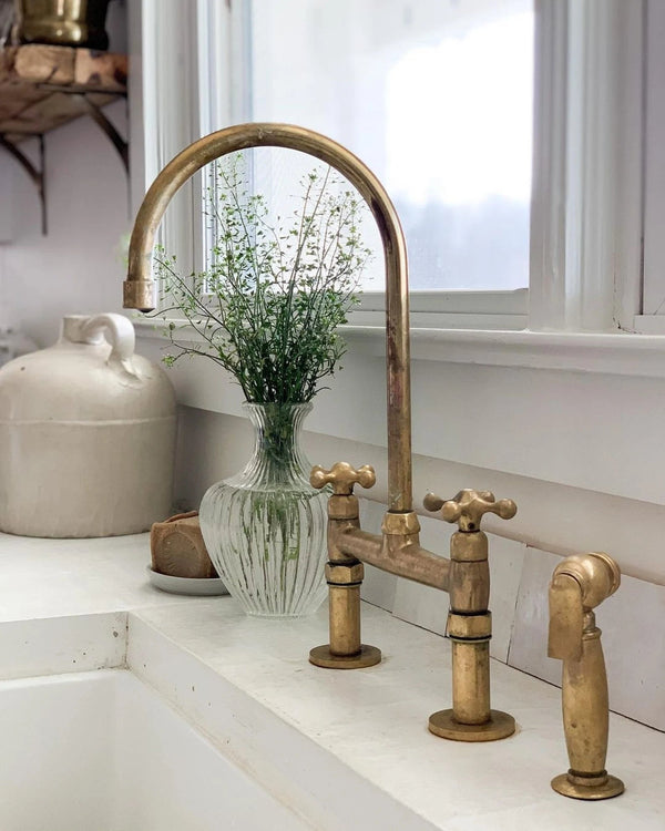 Unlacquered brass bridge faucet with cross handles installed in a kitchen