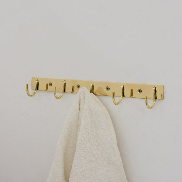Solid brass coat hooks rack wall mounted, showing the rich warm tone of natural unlacquered brass in a hallway setting